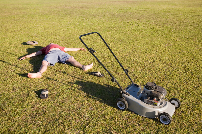 Man laying spread eagles on his back, flip-flops off, arms extended, feigning exhaustion while lawn mowing.
