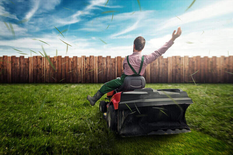 Man wearing suspenders, right hand extended in the air, as he rides his lawn tractor. Best time to mow your yard is when you have time to do it and enjoy it.