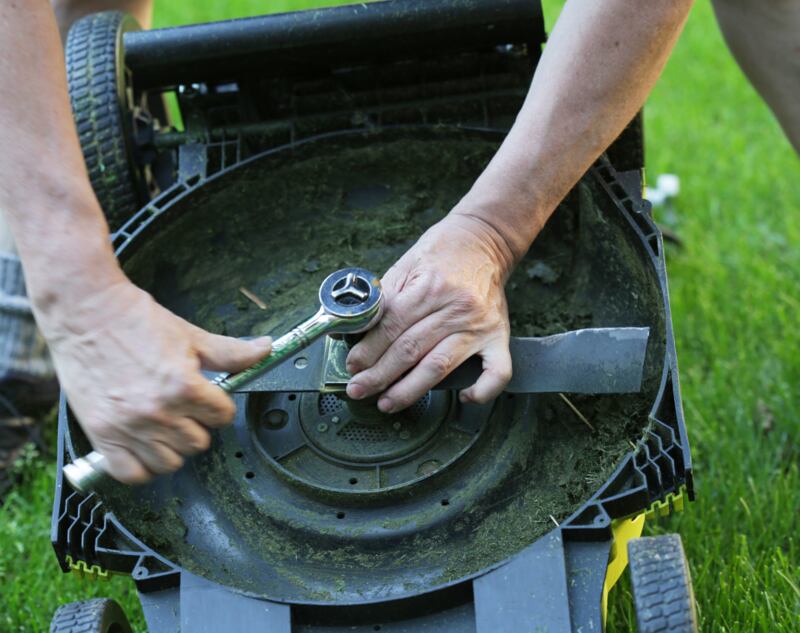 A DIY worker replacing a blade of a lawn mower