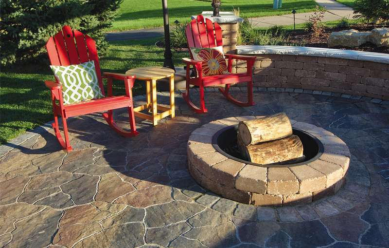 A fire pit on a patio with two red chairs and a mini table next to it